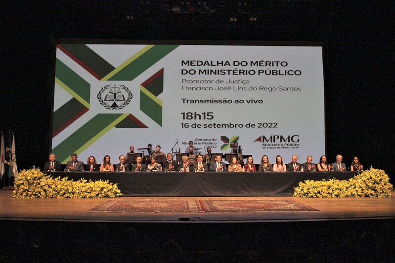 foto horizontal mesa de honra com 20 pessoas sentadas e ao fundo um painel com a descrição medalha do mérito do ministério público promotor de justiça Francisco José Lins do Rego Santos.