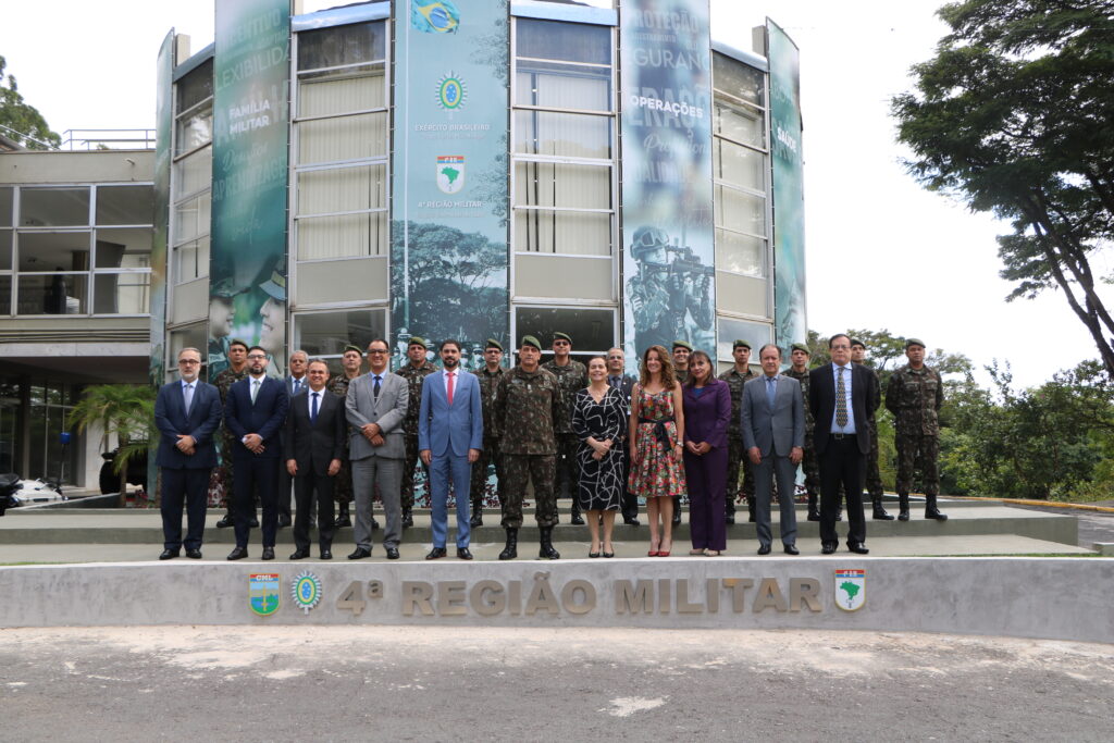 Foto horizontal, colorida, com um grupo de pessoas, homens e mulheres, posando para a foto em frente ao prédio da 4ª Região Militar.