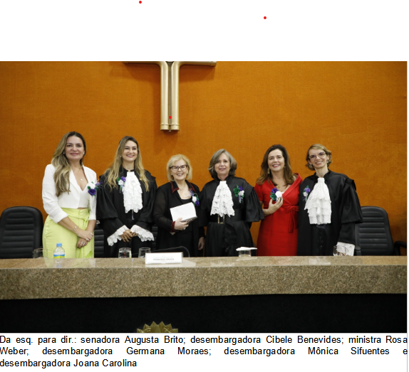 Foto horizontal colorida com seis mulheres em pé, atrás da mesa de honra da solenidade. 