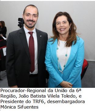 Foto colorida vertical mostra o Procurador-Regional João Batista ao lado da desembargadora Mônica Sifuentes. Os dois estão de pé olhando para a câmera.