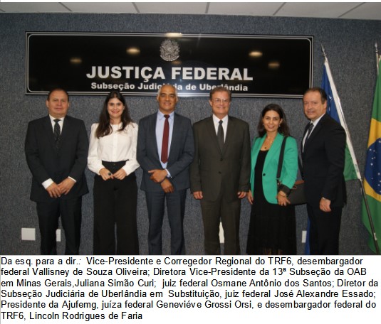 Foto colorida horizontal mostra as autoridades participantes do evento de pé em frente à placa da Justiça Federal de Uberlândia. Na fotografia, aparecem quatro homens e duas mulheres.