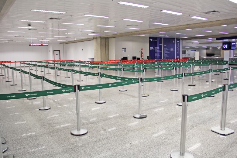 Fotografia retangular e colorida em que  aparecem barreiras metálicas com faixas da Receita Federal num aeroporto.