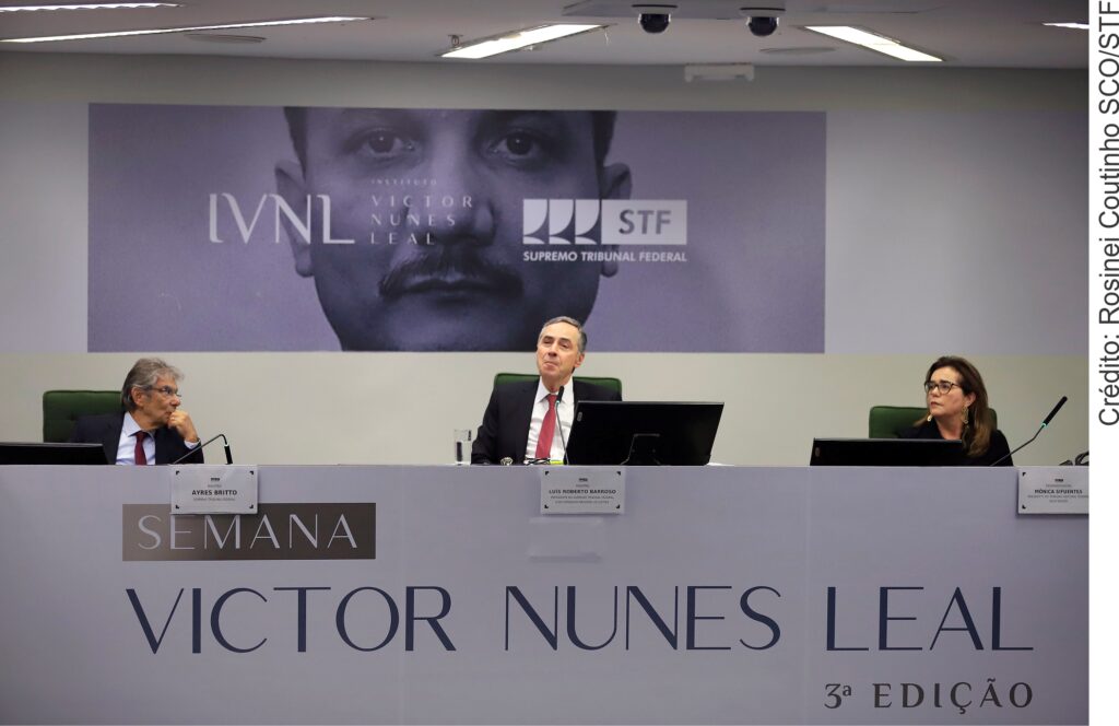 Fotografia colorida em que aparecem dois homens e uma mulher em uma mesa. À frente, o seguinte texto: "Semana Victor Nunes Leal".