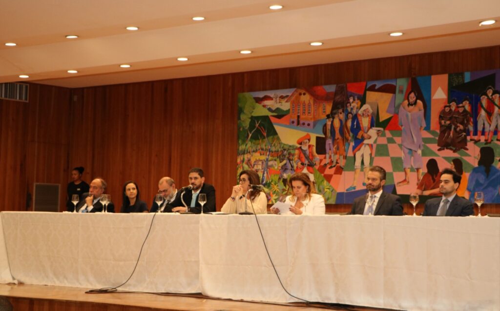 Fotografia colorida horizontal da mesa de honra do seminário “As ciências criminais nos 35 anos da Constituição Federal” com cinco homens e duas mulheres.