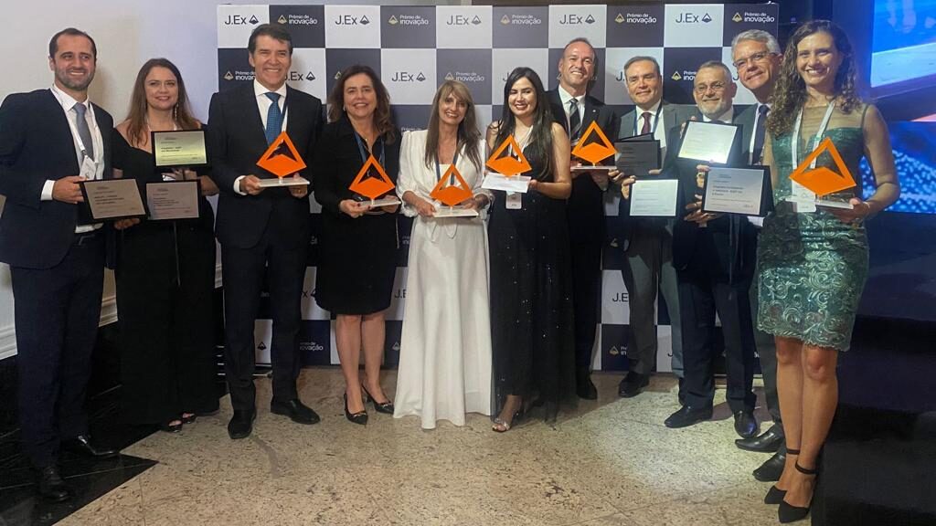 Fotografia colorida horizontal de um grupo de pessoas segurando o "Prêmio de Inovação J.Ex".