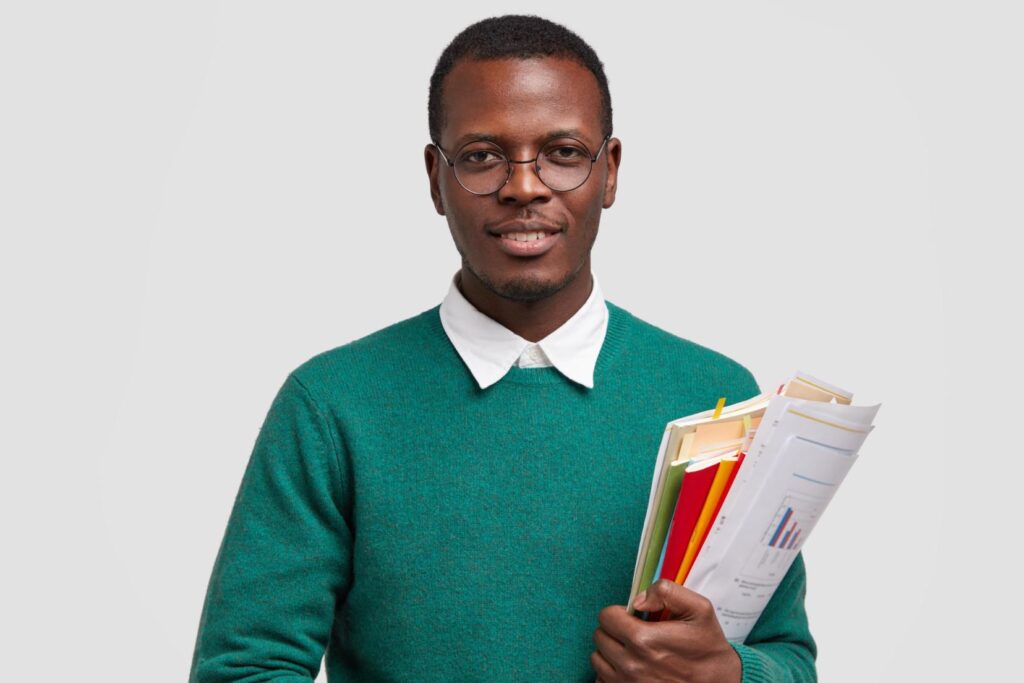 Imagem colorida de um homem negro segurando vários livros na mão esquerda.
