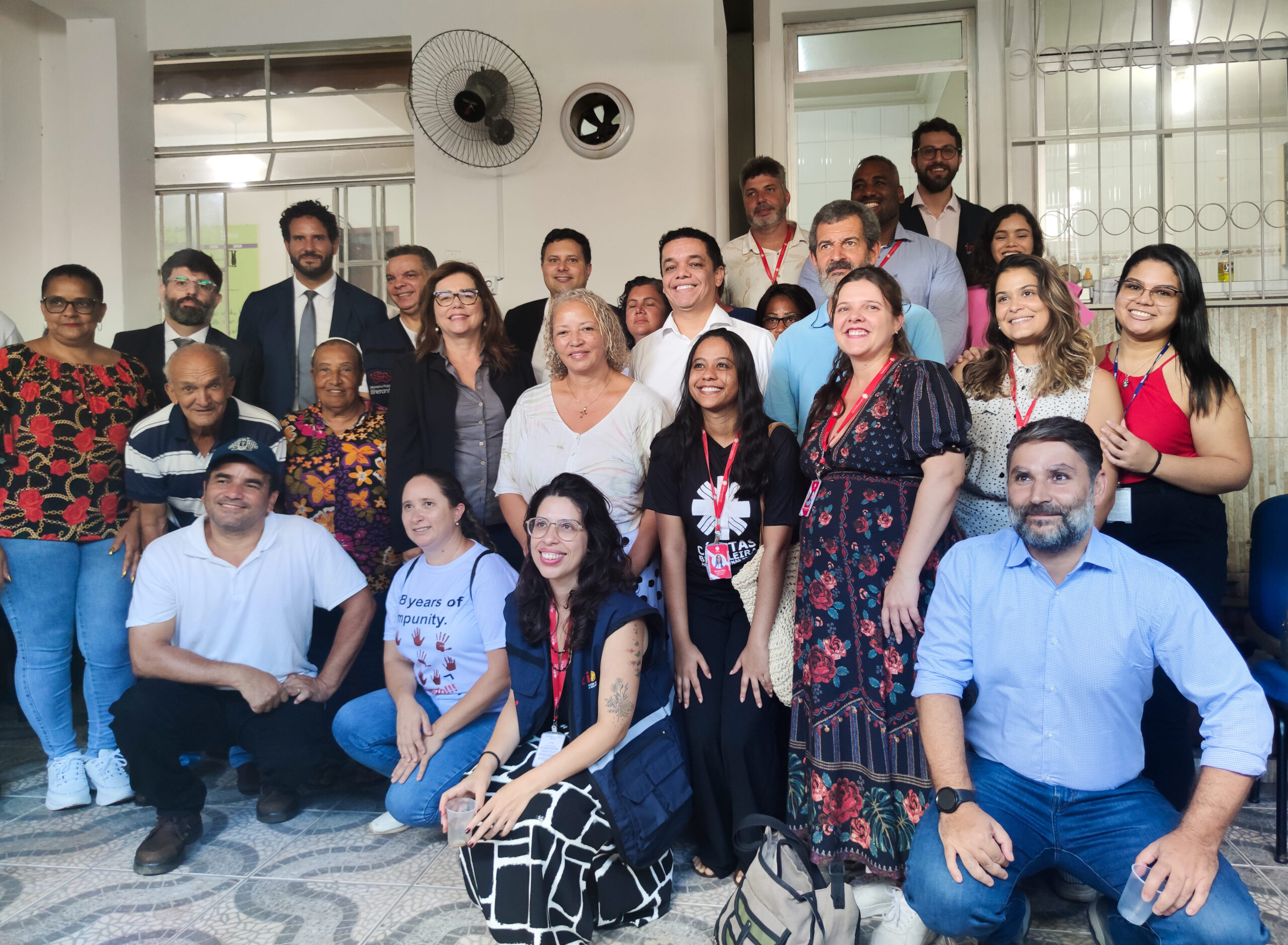 Fotografia colorida de um grupo de pessoas reunidos para uma foto. Legenda: Comitiva visitou sede da Comissão de Atingidos, em Mariana.