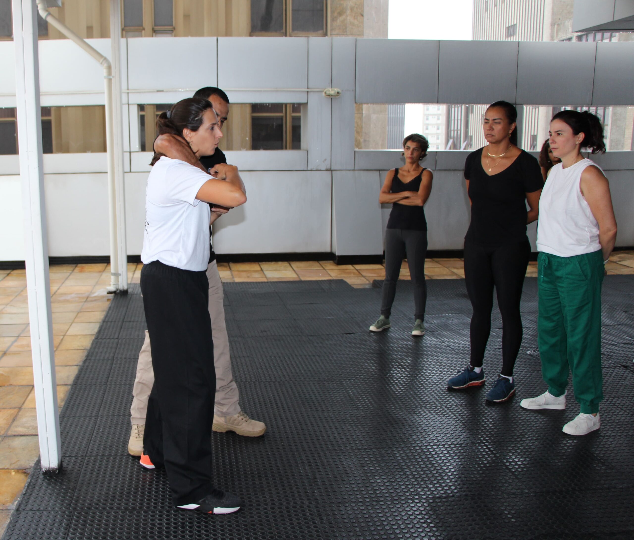 Fotografia colorida da instrutora Fernanda Sampaio ensinando artes marciais para um grupo de mulheres.