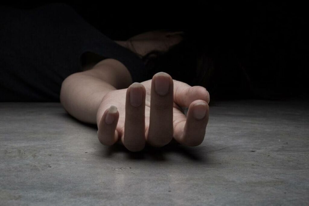 Fotografia colorida de uma mulher caída no chão com a mão esticada.
