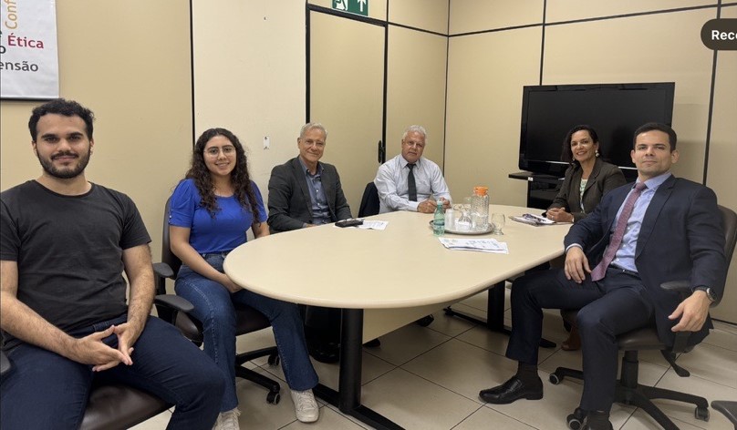 Quatro homens e duas mulheres sentados em torno da mesa de reunião.