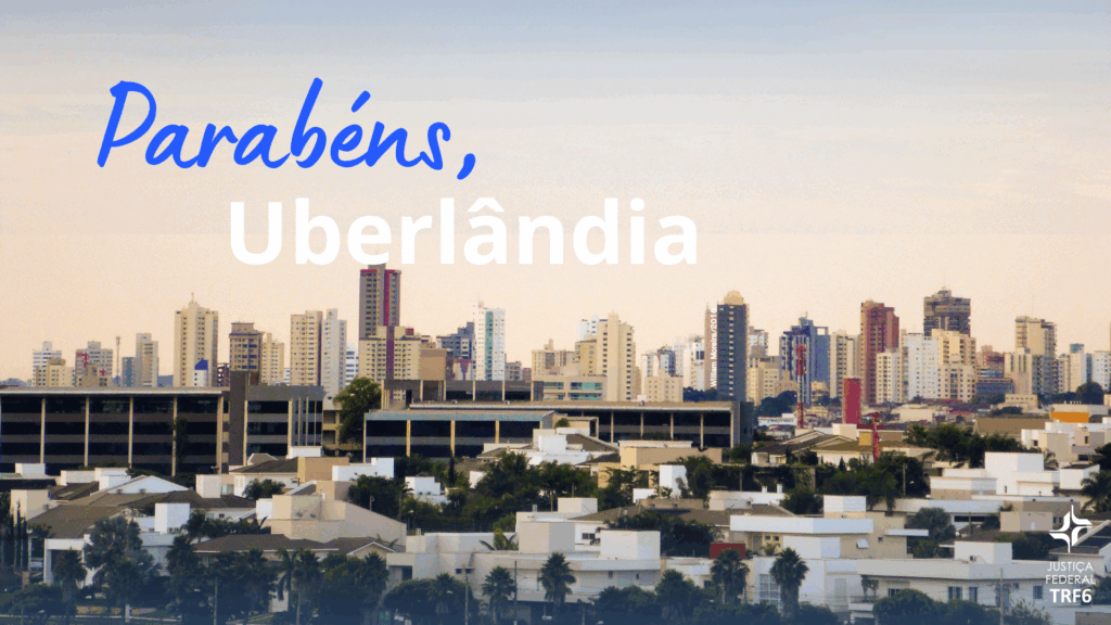 A imagem é um cartão de felicitações com uma vista panorâmica da cidade de Uberlândia, Minas Gerais, ao entardecer. No canto superior esquerdo, a frase "Parabéns, Uberlândia" está escrita em letras brancas, com a palavra "Parabéns" em uma fonte mais informal e azul. No canto inferior direito, o logotipo da "JUSTIÇA FEDERAL TRF6" está em um tom de branco. A imagem mostra diversos prédios altos e residenciais em primeiro plano, com um céu claro e suave.
