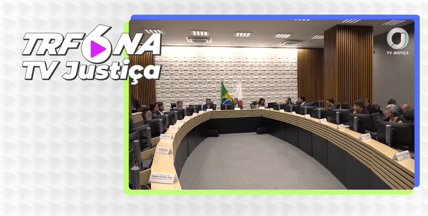 A imagem é uma captura de tela de uma transmissão da TV Justiça, com o logotipo "TRF6 NA TV Justiça" no canto superior esquerdo. O quadro principal, que tem uma borda de cores vibrantes, mostra uma visão panorâmica de uma sala de audiência.

No centro da sala, há uma grande mesa em formato de semicírculo, onde várias pessoas, incluindo homens e mulheres, estão sentadas. Atrás da mesa, há uma parede com um padrão texturizado e, no centro, as bandeiras do Brasil e de Minas Gerais. O ambiente é bem iluminado, com iluminação no teto, e o chão é cinza.