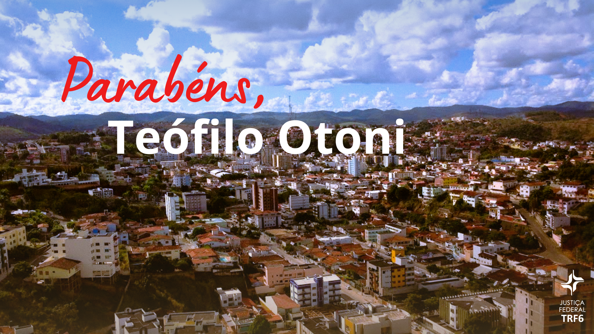 Esta é uma fotografia aérea de Teófilo Otoni, com muitas construções e colinas ao fundo sob um céu azul com nuvens. Sobreposta à paisagem, há uma mensagem de celebração. O texto em destaque em vermelho e branco diz "Parabéns, Teófilo Otoni". No canto inferior direito, há o logotipo da Justiça Federal TRF6.