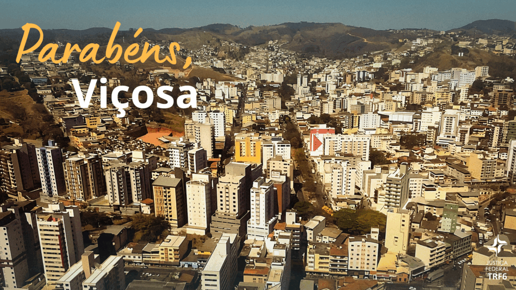 Foto panorâmica aérea da cidade de Viçosa, mostrando uma paisagem densa com múltiplos edifícios residenciais e comerciais, cercados por colinas e vegetação no horizonte.

No canto superior esquerdo, em uma fonte cursiva amarela e branca, há a mensagem: "Parabéns, Viçosa".

No canto inferior direito, está o logotipo da Justiça Federal TRF6.