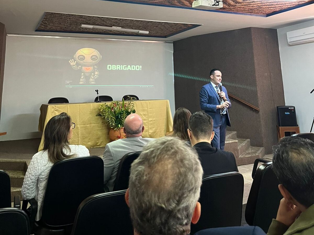 Um homem, vestido de forma formal, está falando para uma audiência sentada. O slide no fundo exibe a palavra "OBRIGADO!".