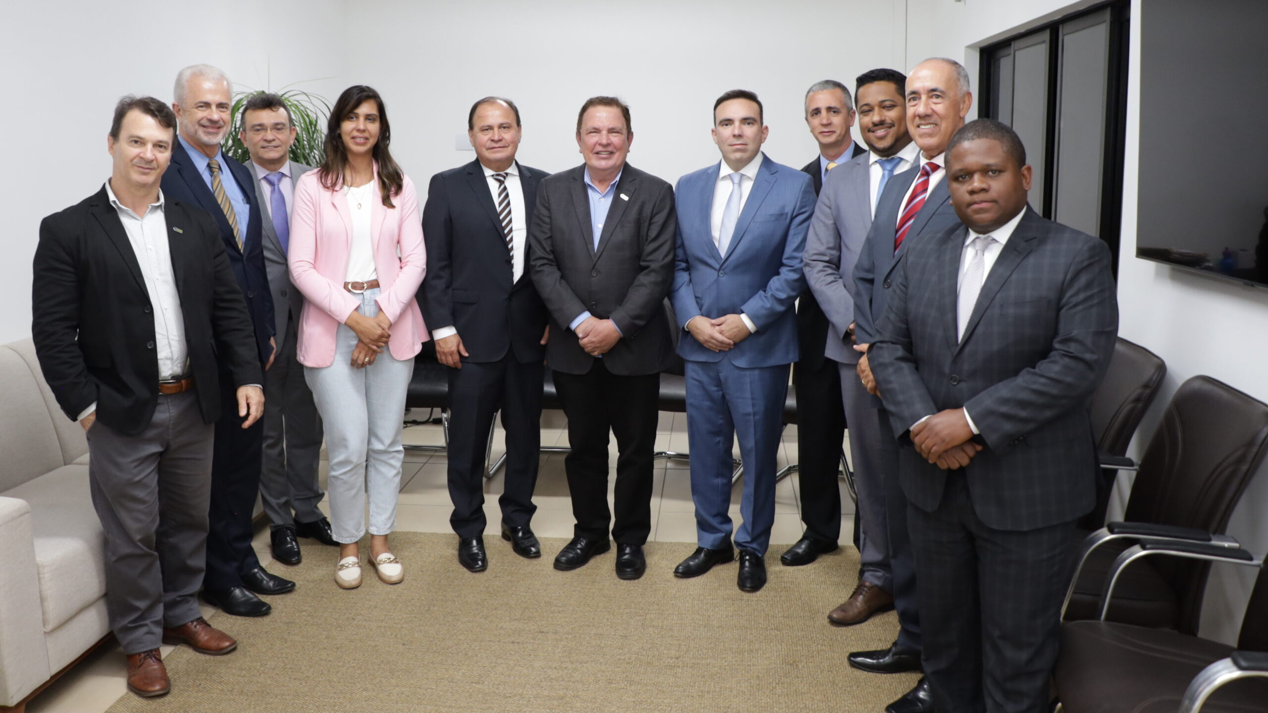 Um grupo de onze pessoas (dez homens e uma mulher) está posando em pé em um escritório ou sala de reunião. O grupo está vestido com trajes de negócios; a maioria usa terno e gravata.

O ambiente tem paredes claras, um sofá claro à esquerda e cadeiras escuras à direita.