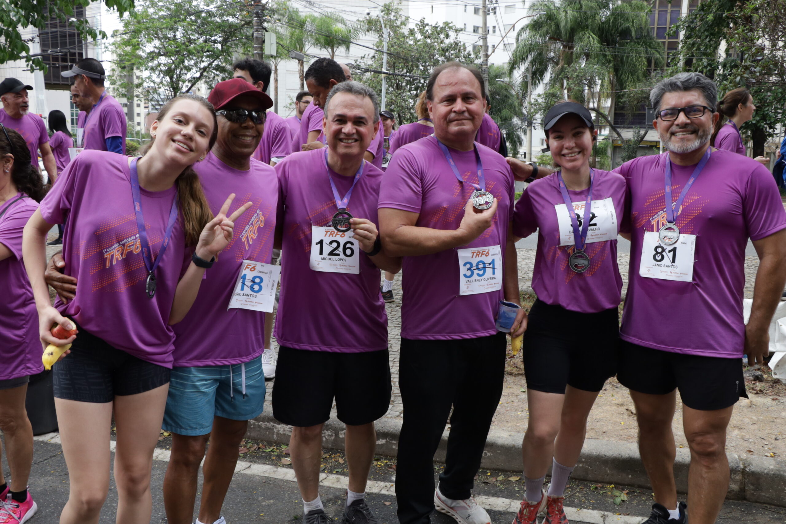 Seis corredores em camisetas roxas, com números de peito e medalhas, sorriem e posam juntos.