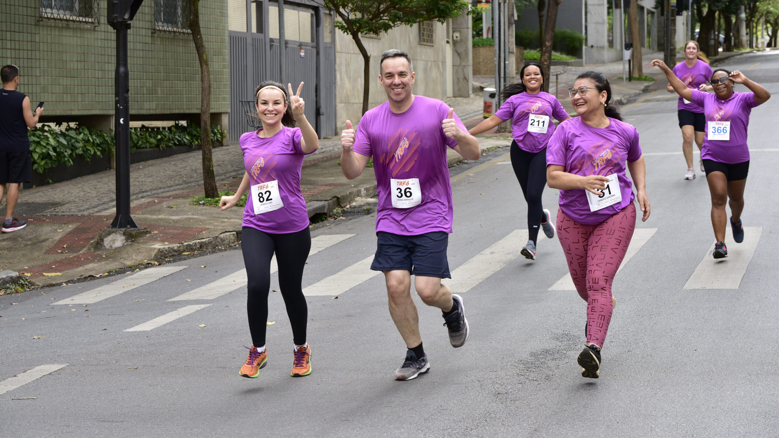 Quatro corredores em camisetas roxas sorriem, correm na rua e gesticulam em celebração.