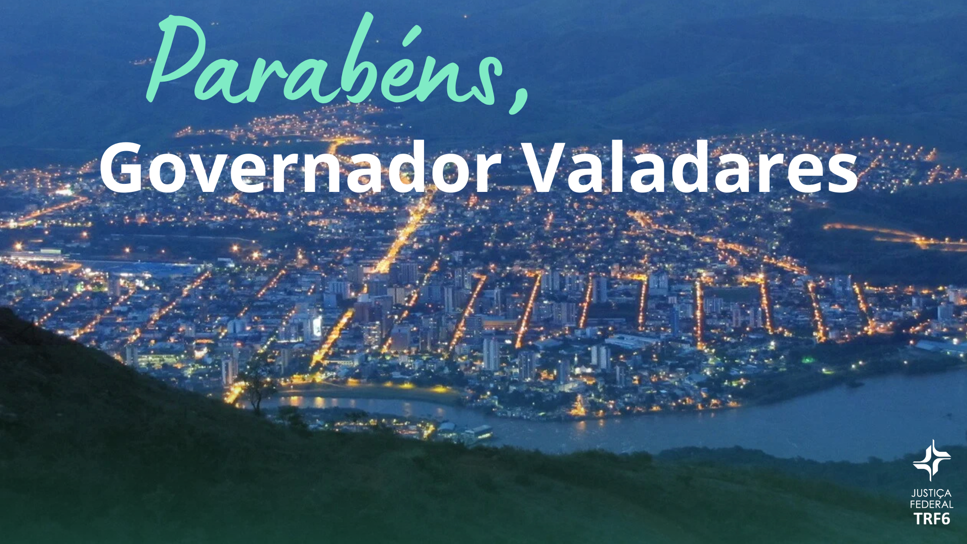 Vista panorâmica noturna da cidade de Governador Valadares, com luzes urbanas e o Rio Doce em destaque. Sobre a imagem, o texto "Parabéns, Governador Valadares" e o logotipo da Justiça Federal do TRF6.