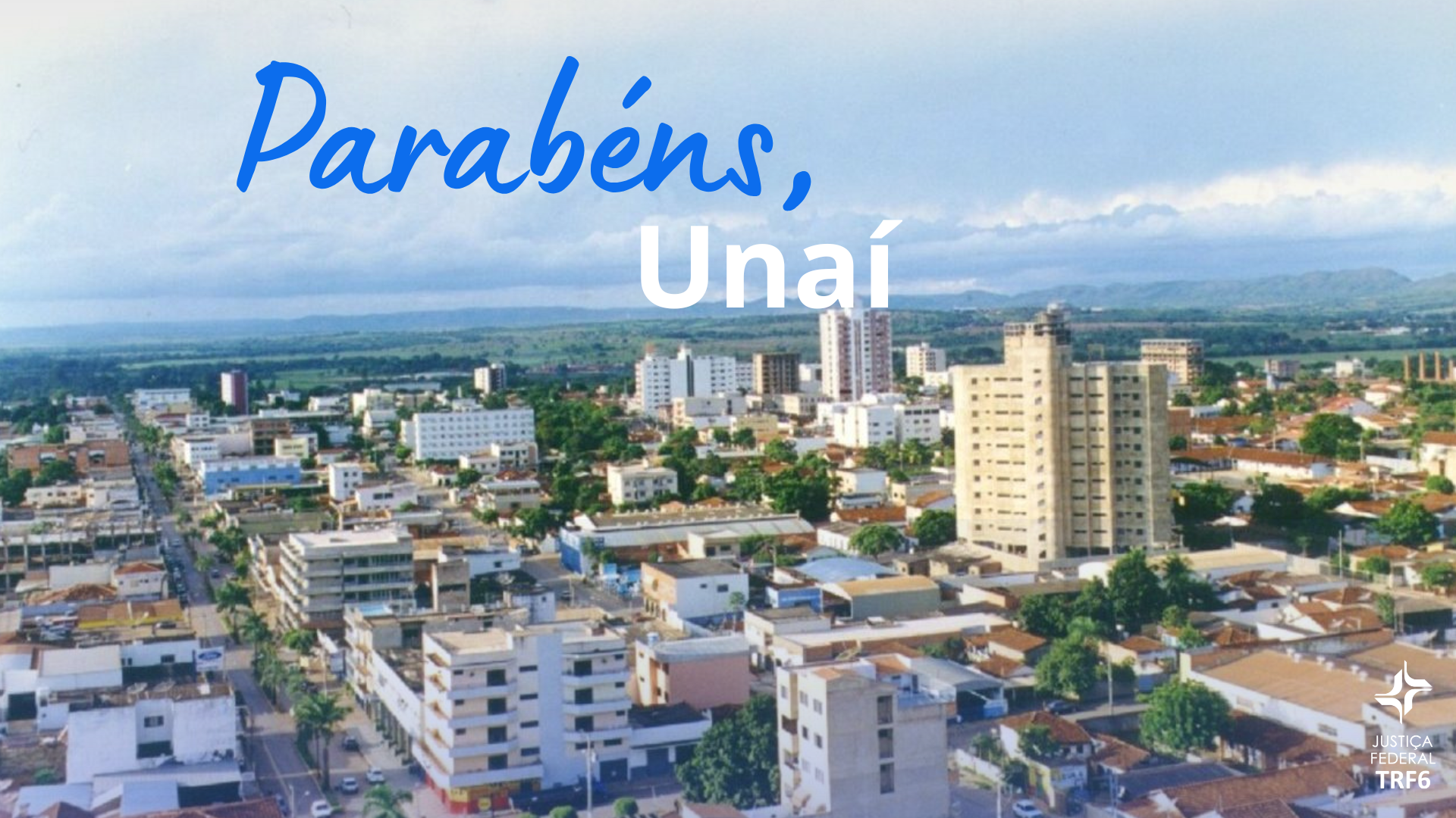 Uma vista aérea da cidade de Unaí apresenta diversos prédios e casas sob um céu nublado, com montanhas ao fundo. O texto "Parabéns, Unaí" aparece em destaque no topo, escrito em azul e branco, enquanto o logotipo da Justiça Federal TRF6 está posicionado no canto inferior direito.