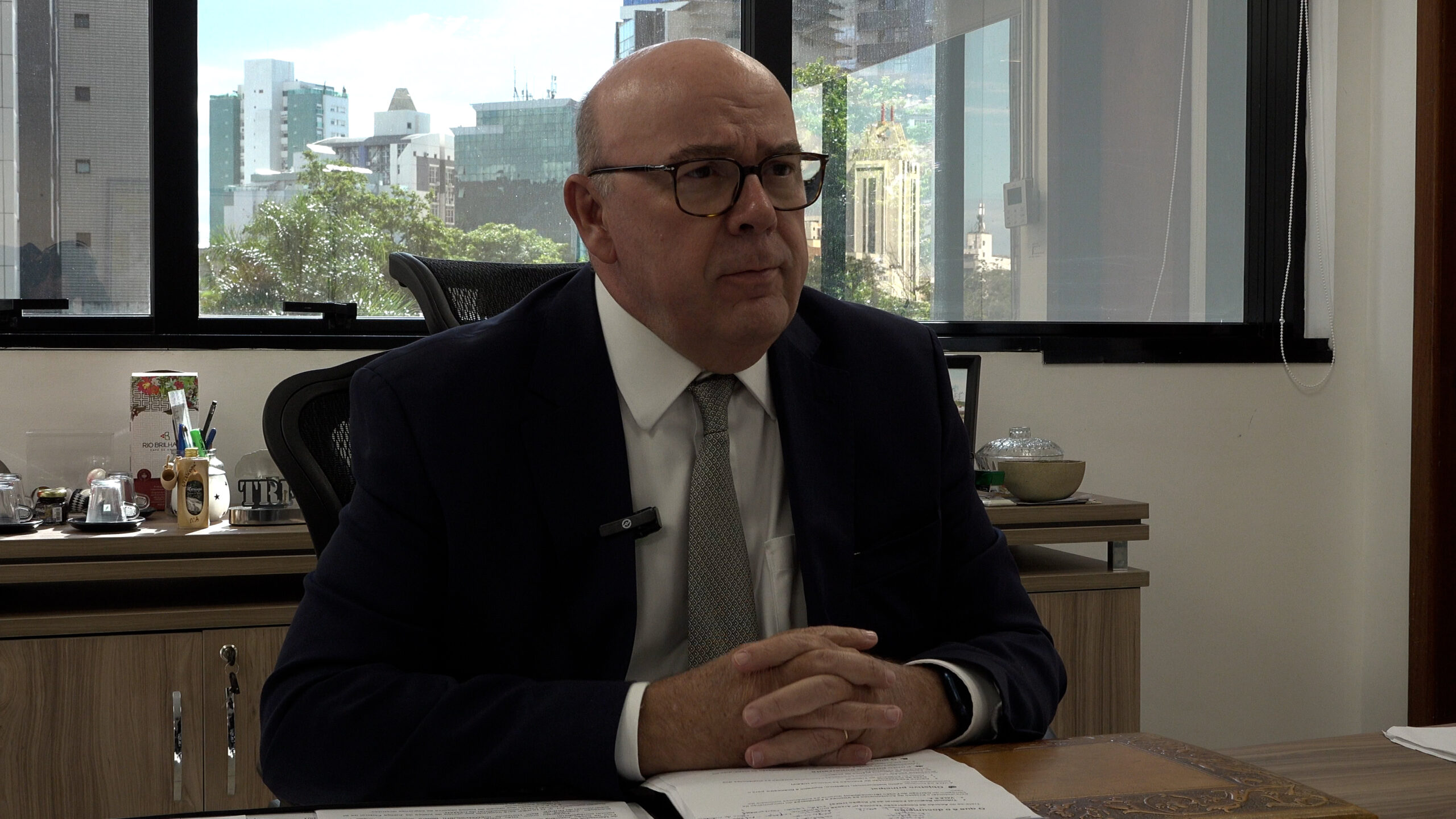 Retrato formal do Desembargador Federal Vallisney Oliveira, atual Presidente do TRF6 (biênio 2024-2026). Ele veste um terno azul-marinho, camisa branca e gravata escura com listras, posando contra um fundo cinza neutro.